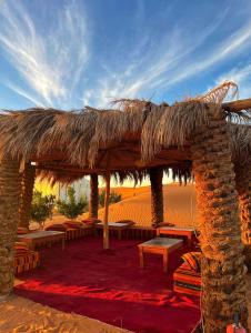 a straw hut with tables and benches in the desert at desert indigo luxury camp in Merzouga