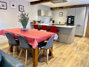 uma cozinha com uma mesa com cadeiras vermelhas e uma cozinha com armários brancos em Stunning 3-Bed Cottage in The Forest of Dean em Coleford