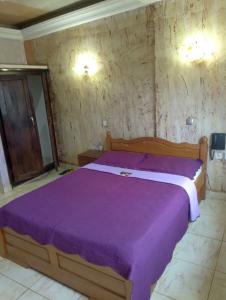 sypialnia z łóżkiem z fioletową narzutą w obiekcie CONSTELLATION HOTEL w mieście Dschang