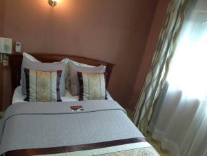 Cama con cabecero de madera y almohadas en CONSTELLATION HOTEL, en Dschang