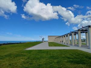 a building on a field with a blue sky and clouds at Maison bord de mer in Asnelles