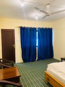 a room with blue curtains and a bed and a table at Hotel Travel Lodge in Skardu