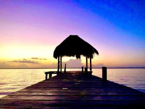 a pier with an umbrella on the water at sunset at Cabaña Sofía Bacalar in Bacalar