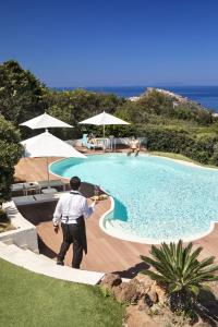 un homme debout en face d'une piscine dans l'établissement Il Borgo BagaBaga - Exclusive Country Retreat, à Castelsardo