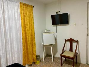 a room with a yellow curtain and a chair and a television at Habitación Cerca de aeropuerto in Cartagena de Indias