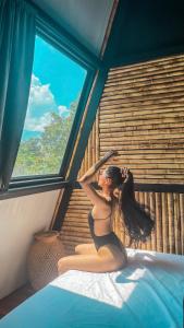a woman sitting on a bed looking out a window at Cabaña 25km de Medellín, Benevento Glamping in Girardota