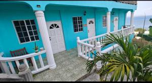 a blue house with a white porch and the ocean at Isla Vista Apartment Canouan in Canouan