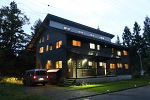 une maison noire avec une camionnette garée devant elle dans l'établissement Bears Den Mountain Lodge, à Hakuba