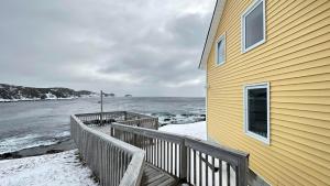 a yellow house with a wooden deck next to the water at Victoria Cottage in Twillingate