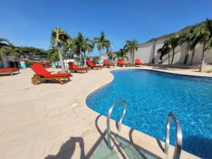 a swimming pool with red lounge chairs and palm trees at Hotel Med Taganga in Taganga