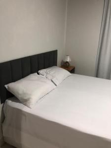 a white bed with a black headboard and two white pillows at Quarto privativo 01 in Sinop
