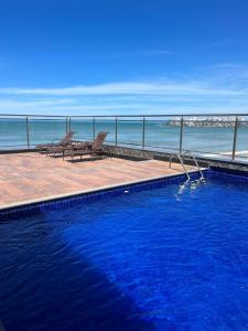 a swimming pool with two chairs next to the ocean at Hotel Quatro Estações in Guarapari