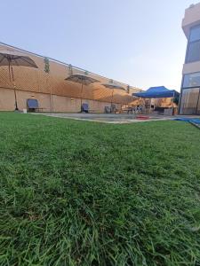 a field of grass in front of a building with umbrellas at Villa rotana airport road in Al Qasţal