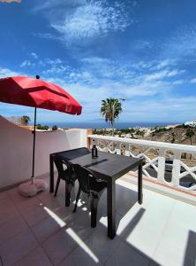 un tavolo nero con ombrellone rosso sul balcone di Studio vista oceano in Costa Adeje ad Adeje