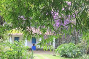una casa bianca con porte blu e alberi viola di Chalé na floresta com varanda a Ouro Preto