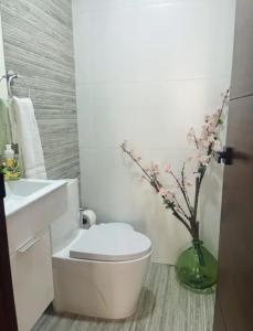 baño con aseo blanco y jarrón con flores en Santuario Home, en Santo Domingo