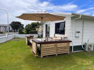 a patio with an umbrella and a table and benches at Kopu Cottage - in the heart of Raglan. in Raglan