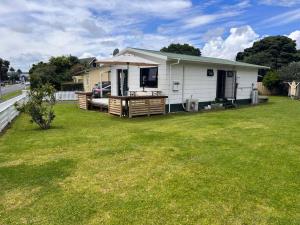a small white house with a porch and a yard at Kopu Cottage - in the heart of Raglan. in Raglan