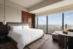 Shangri-La Nanning - The tallest hotel worldwide in Shangri-La Group في نانينغ: غرفة نوم بسرير ابيض كبير ونوافذ كبيرة