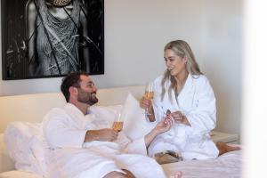 Un uomo e una donna seduti a letto a bere champagne di Amarè Beachside Luxury a Turners Beach