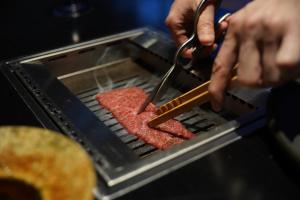 eine Person, die Fleisch auf einem Grill mit einer Schere kocht in der Unterkunft Nazuna Kyoto Tsubaki St. in Kyoto