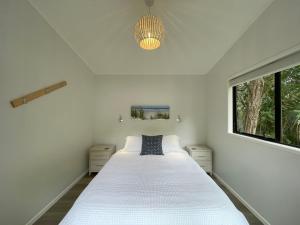 a bedroom with a white bed and a window at Tui Cottage - Waiheke Escapes in Onetangi