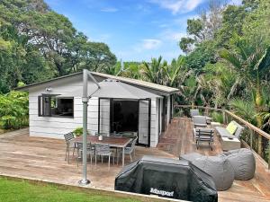 a house with a deck with a table and an umbrella at Tui Cottage - Waiheke Escapes in Onetangi