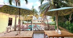 A'Famosa Bungalow*Private Garden Stage*22Pax*NEW في Kampong Ulu Pegoh: طاولتان خشبيتان مع مظلات أمام منزل