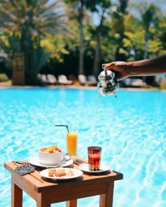 a person holding a tea kettle over a table next to a pool at Es Saadi Marrakech Resort - Palace in Marrakech