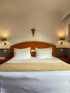 uma cama com lençóis brancos e uma cruz na parede em Hotel Santo Amaro - SA Hotels em Fátima