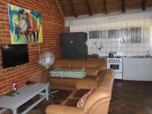 a living room with a brown leather couch and a kitchen at Marico Guest Lodge in Groot-Marico