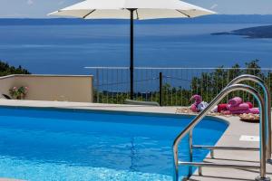 a swimming pool with an umbrella and some dolls at Holiday home Marta with heated pool,grill,sea view in Bast