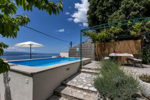 a swimming pool in a backyard with a table and an umbrella at Holiday home Marta with heated pool,grill,sea view in Bast