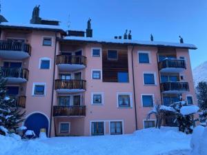 a pink apartment building with snow on the ground at Haus Suot Chesas 8b ÖV Inklusive in Champfer