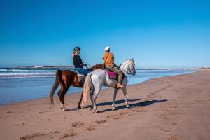 zwei Leute reiten auf Pferden am Strand in der Unterkunft Villa Tazerzit comfort et hospitalité in Essaouira