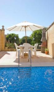 un tavolo con sedie e un ombrellone accanto alla piscina di Villa Harruba a Xagħra