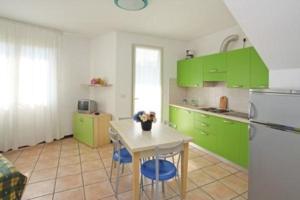 eine Küche mit grünen Schränken, einem Tisch und einem Kühlschrank in der Unterkunft Wohnungen in Ferienanlage in Bibione