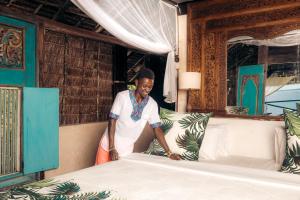 une femme fait un lit dans une pièce dans l'établissement The Cabanas, Anasa Hotels & Experiences, à Matondoni