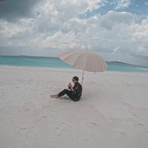 Raalhu Fonu Maldives في Mahibadhoo: رجل يجلس على الشاطئ تحت مظلة