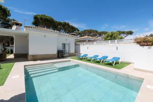 a swimming pool with blue chairs and a house at La Perla Costera in Chiclana de la Frontera