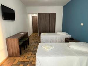 a room with two beds and a desk and a tv at Hotel Quatro Estações in Guarapari