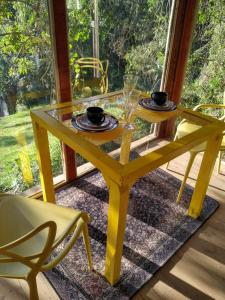 伊塔蒂巴的住宿－Casa de Vidro com cachoeira，一张黄色桌子,上面有两个盘子和玻璃杯