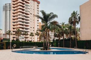 a swimming pool with palm trees and tall buildings at Apartamentos Wayteko Calpe in Calpe