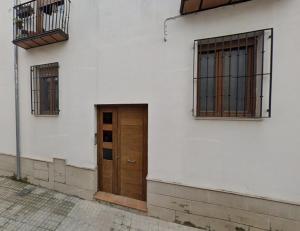 Un edificio blanco con una puerta de madera y dos ventanas. en APARTAMENTO el CARMEN, en Baeza