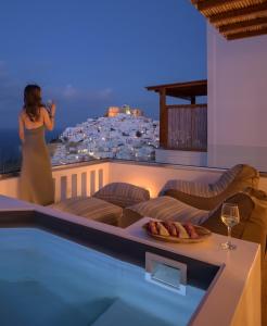 a woman standing on a balcony with a glass of wine at Oneiro Luxury Suites-Adults Only in Astypalaia