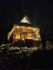 a small house with a thatched roof at night at Wetlands Wayanad Resort with Natural Waterfalls in Padinjarathara