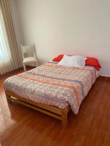 a bed with a comforter and a chair in a room at Habitación cerca a los Pantanos de Villa in Lima