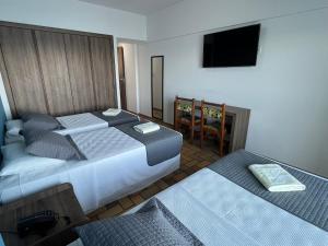 a bedroom with two beds and a flat screen tv at Hotel Quatro Estações in Guarapari