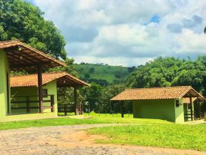 two buildings in a field with trees in the background at Pousada e Camping Recanto da Praia in Capitólio