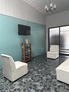 sala de estar con 2 sillas blancas y TV de pantalla plana en Casa Buen Agüero en San Antonio